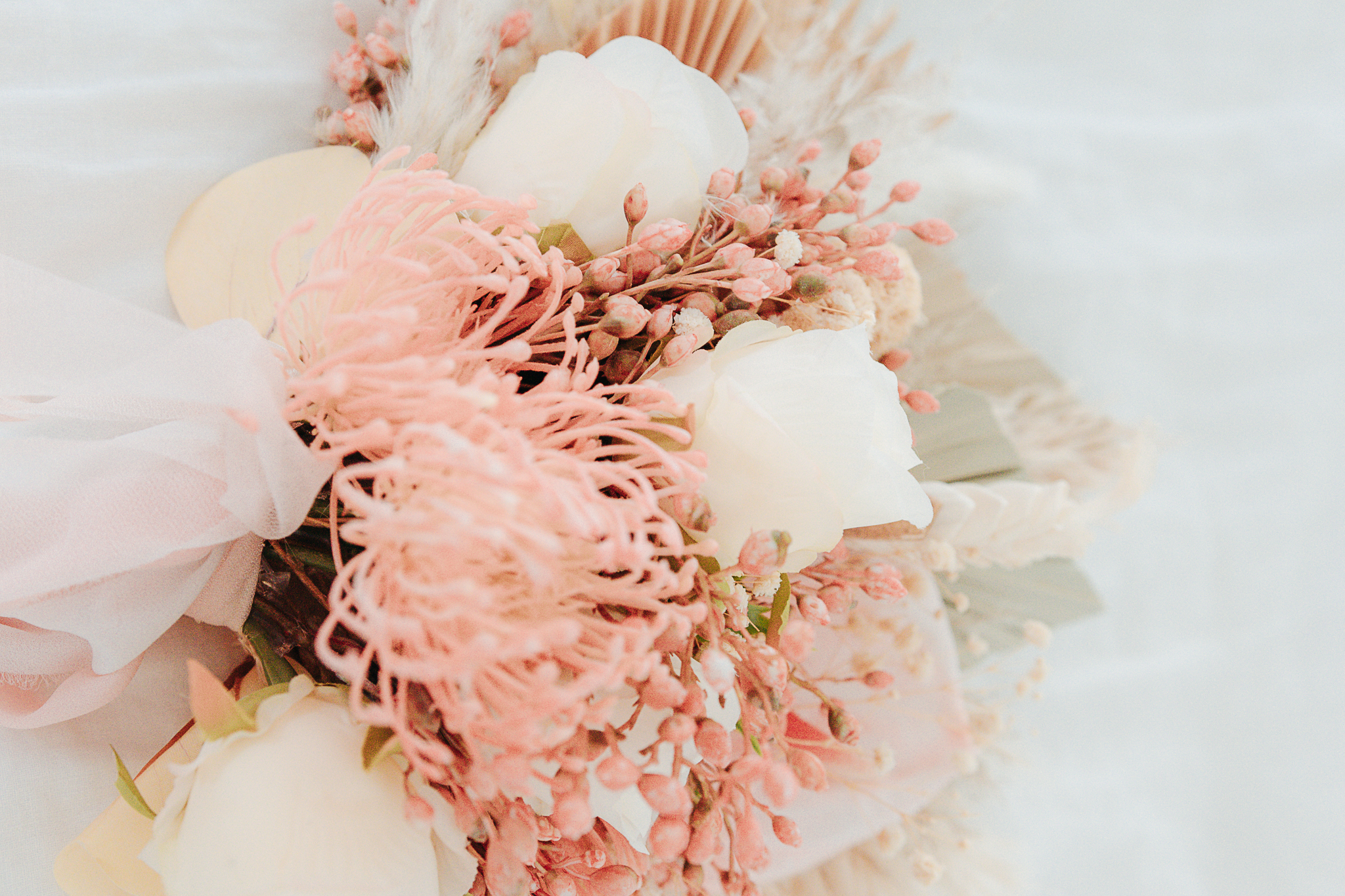 Close-up of a bloom bar bouquet — blush pincushion protea, white roses, and dried botanicals wrapped with soft pink ribbon