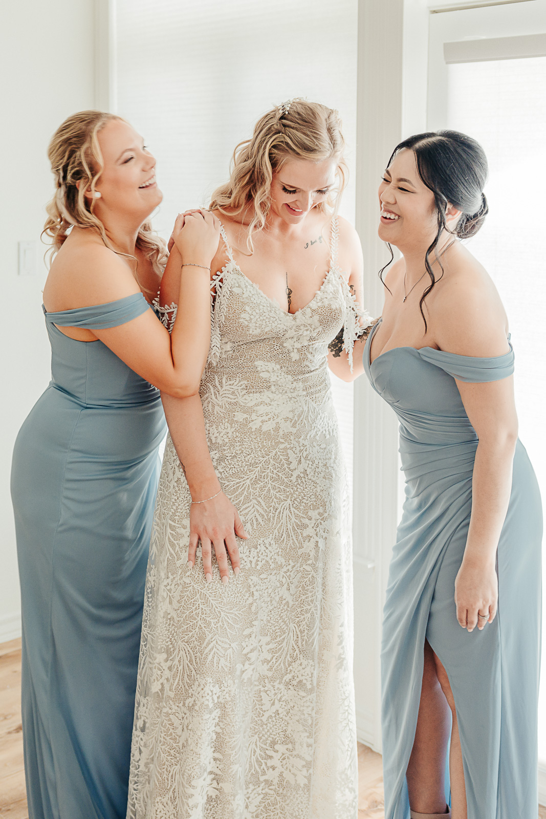 Bride in lace gown laughing with bridesmaids in dusty blue off-shoulder gowns, Hill Country wedding by Weddings by Wendi