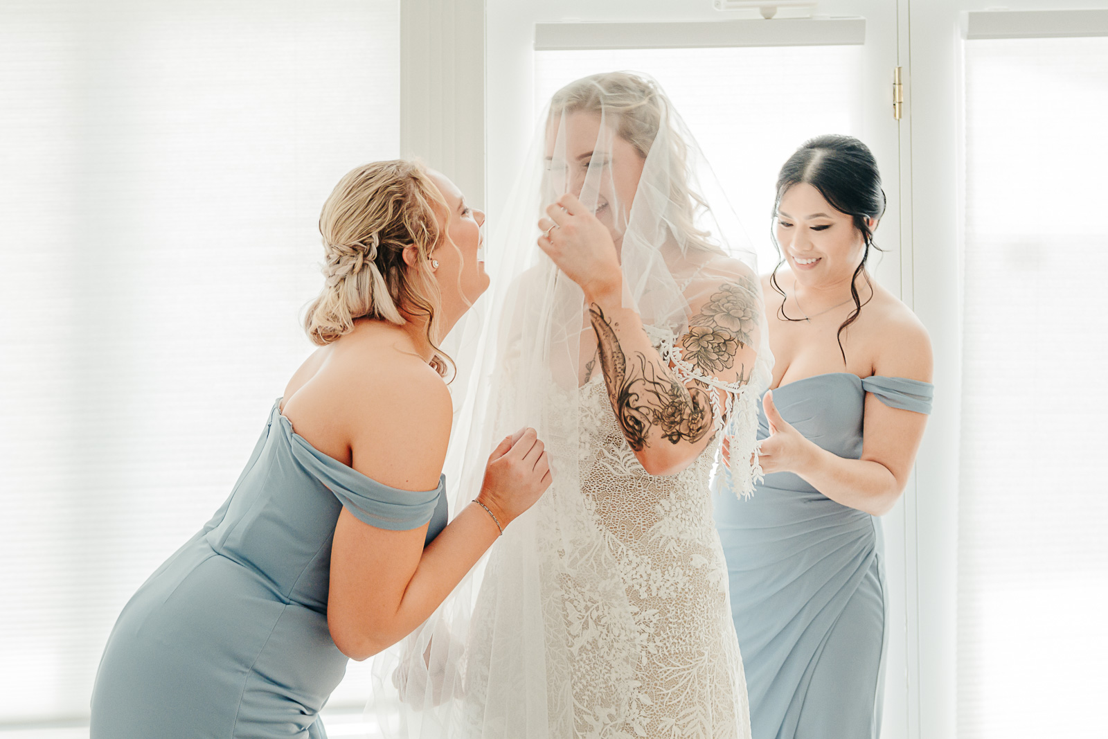 Bridesmaids helping bride with her veil while getting ready, laughing together, coordinated by Weddings by Wendi