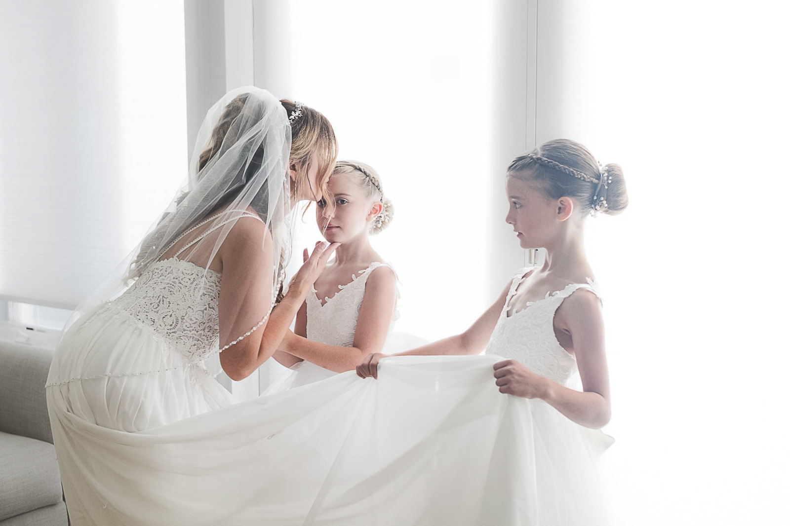 Bride getting ready with flower girls in a bright suite, candid moment photographed by Weddings by Wendi