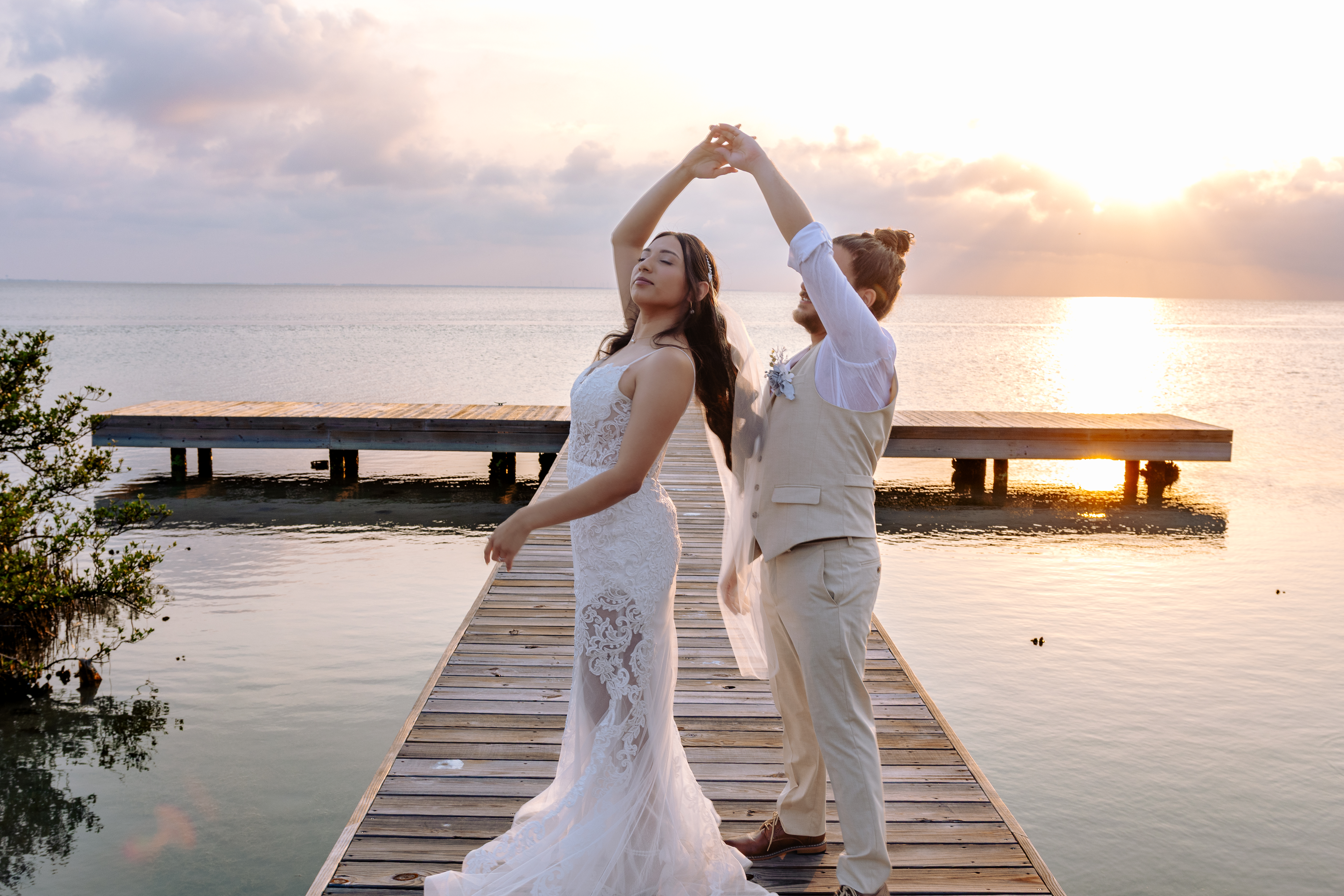 Bride and groom dancing on a wooden dock at sunset over calm water, groom spinning bride with arms raised, photographed by Weddings by Wendi