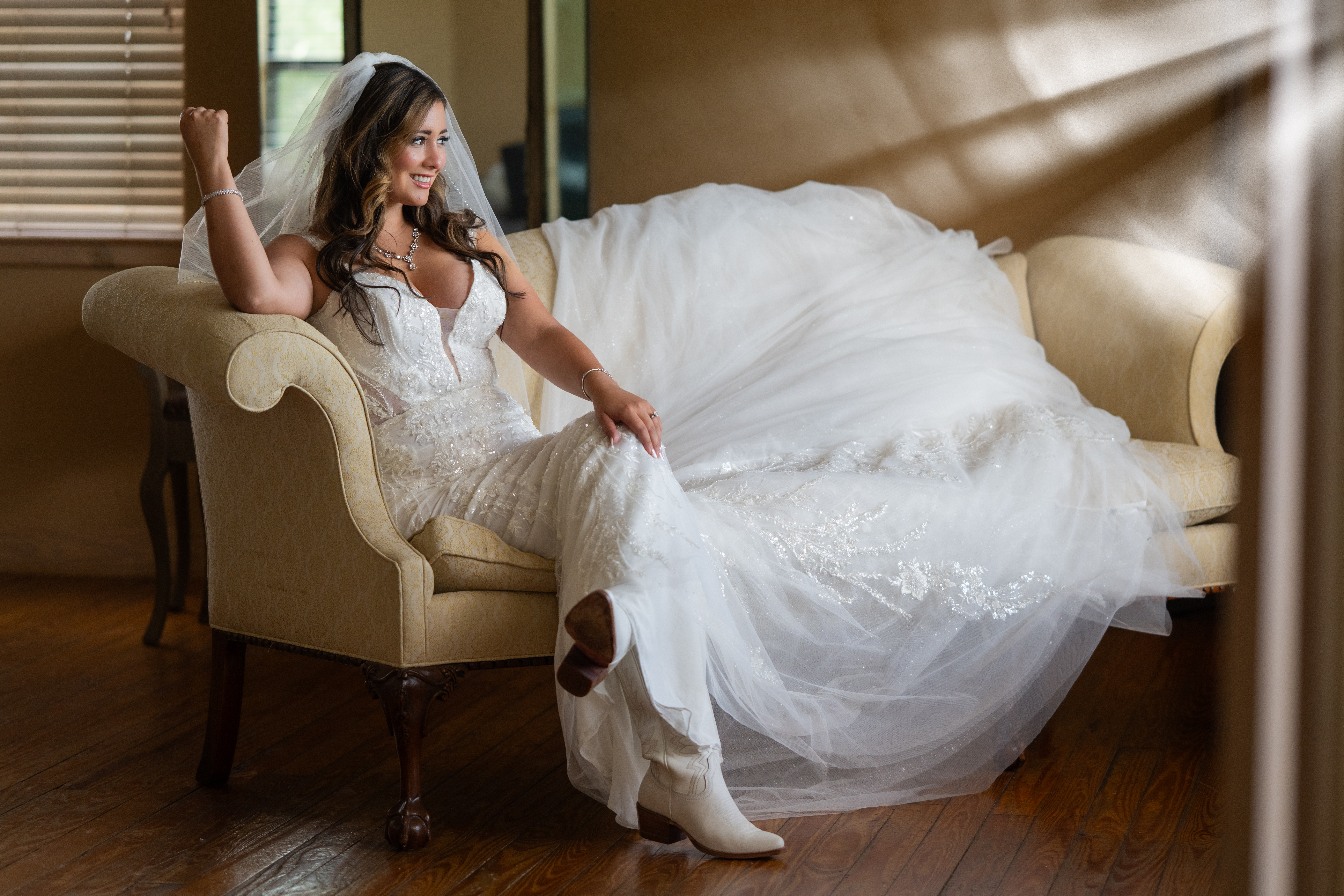 Bride in lace gown and cowboy boots seated on sofa — Memory Lane Ranch wedding venue Dripping Springs Texas