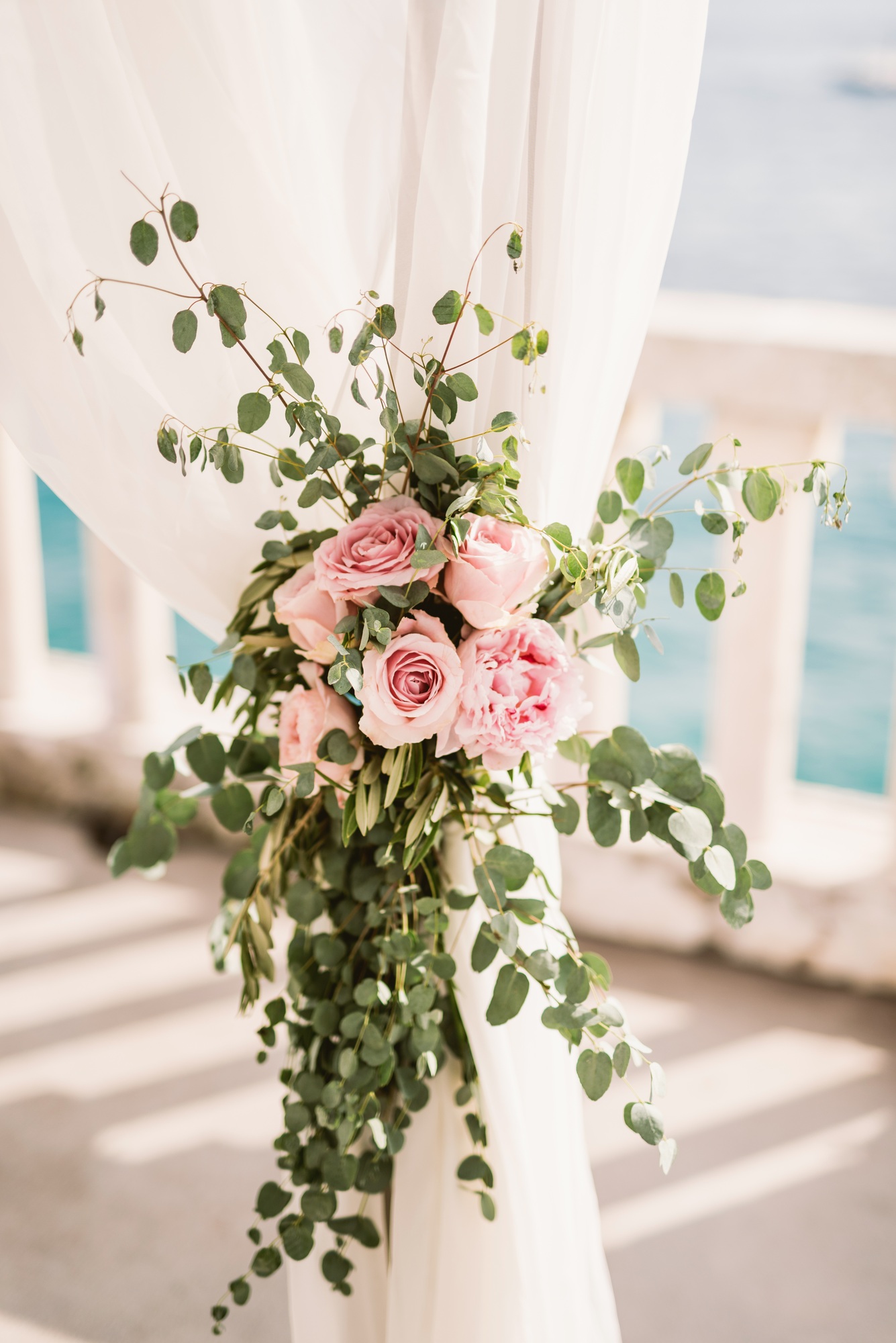 Wedding ceremony arch adorned with pink roses and greenery against a bright outdoor backdrop, coordinated by Weddings by Wendi