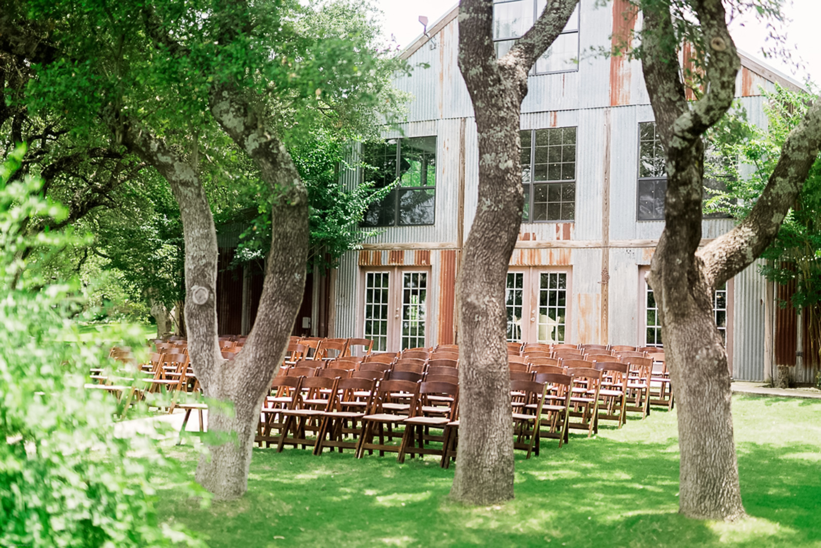 Vista West Ranch outdoor ceremony setup with wooden chairs on the lawn and the rustic corrugated metal barn in the background, Dripping Springs TX
