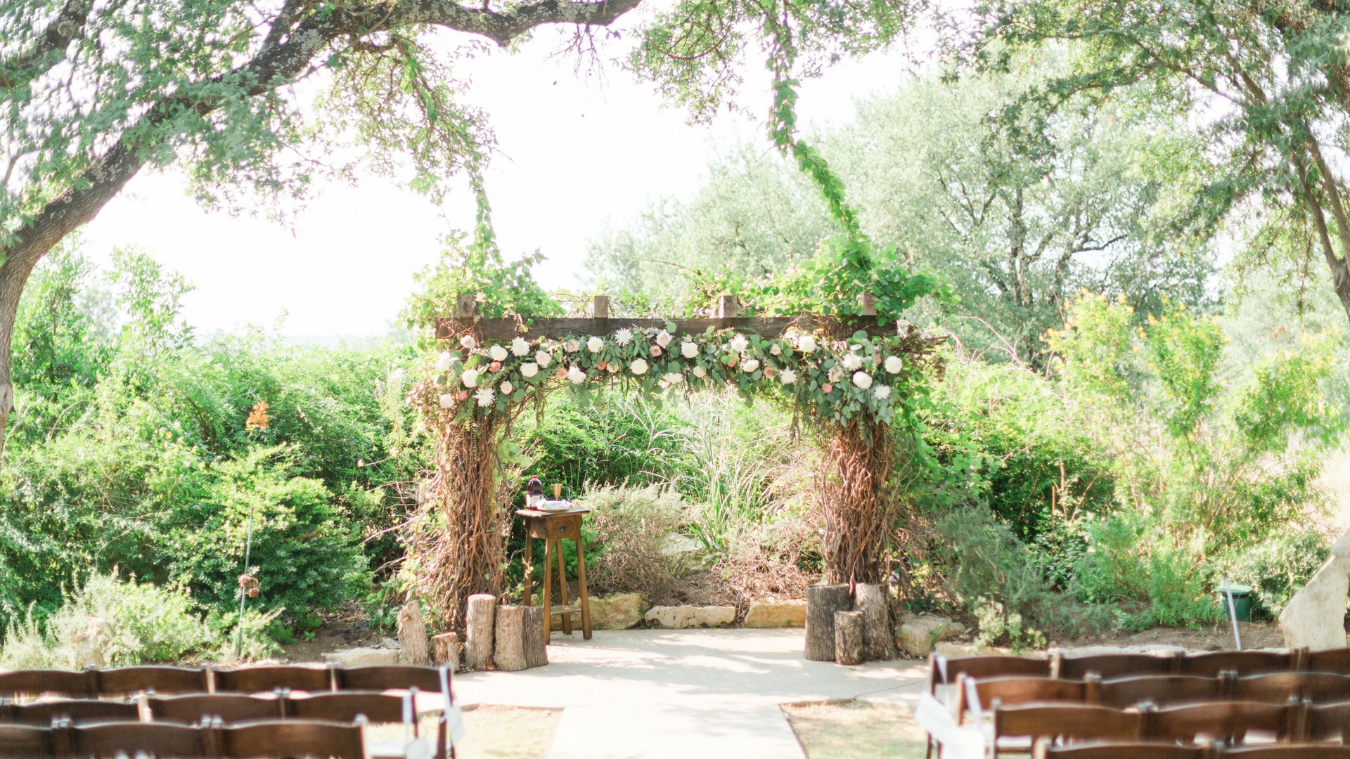 Rustic wooden wedding ceremony arch draped in greenery and blush florals in the Texas Hill Country near Fredericksburg — Weddings by Wendi