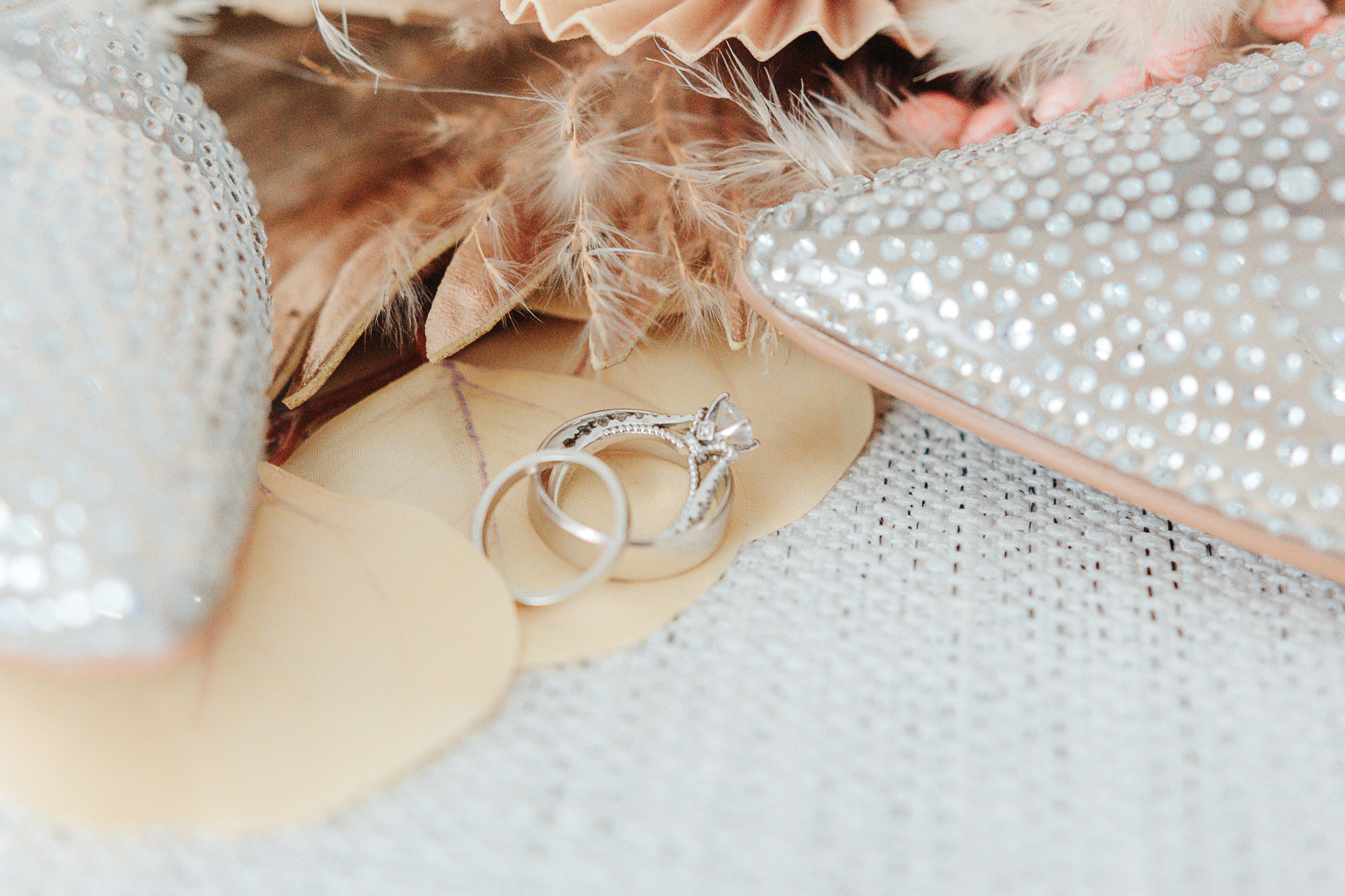 Wedding rings nestled among dried florals and crystal-studded bridal shoes, close-up detail shot by Weddings by Wendi