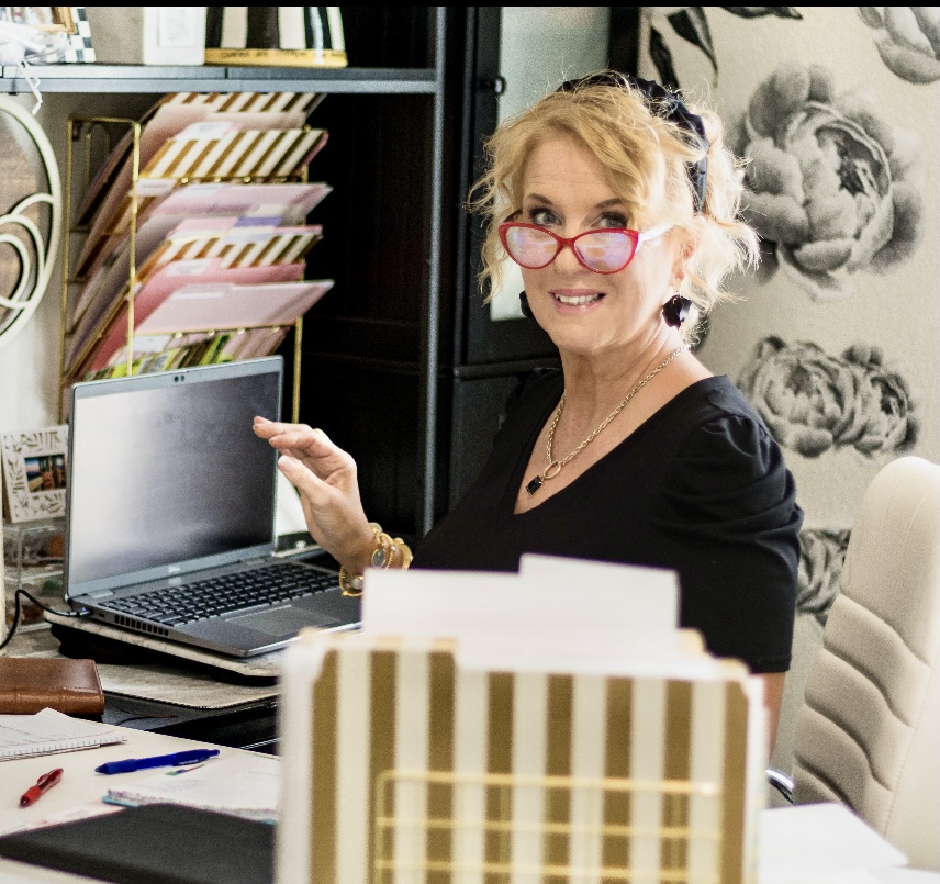 Wendi, Texas Hill Country wedding planner, smiling at her desk surrounded by planning materials and floral wallpaper
