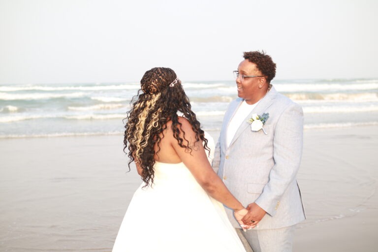 a bride and groom holding hands on the beach