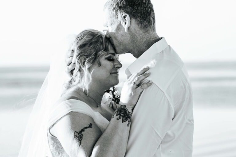 a bride and groom embracing each other on the beach