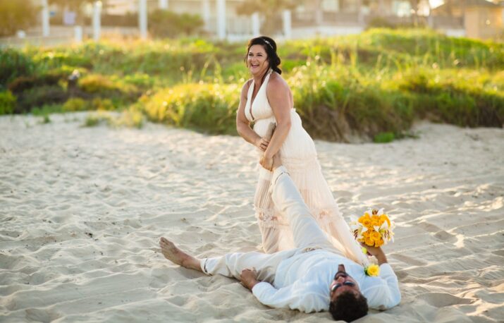 a bride and groom laying on the beach