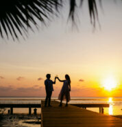 a man and woman standing on a dock at sunset