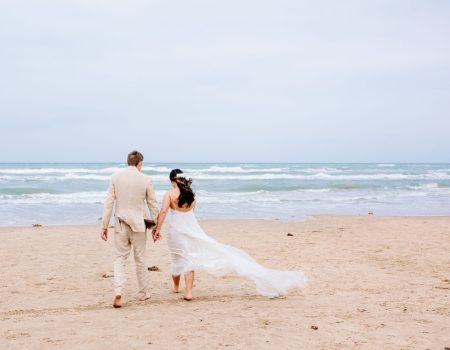 a bride and groom walking on the beach