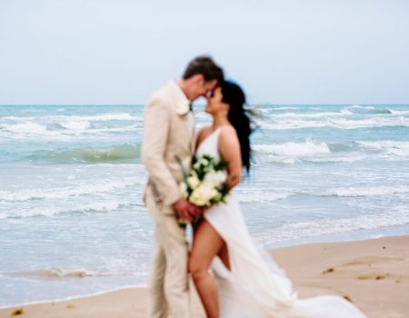 a bride and groom kissing on the beach