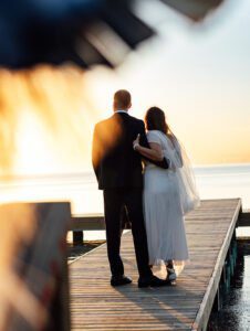 a bride and groom standing on a dock at sunset