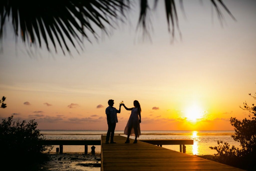 a man and woman standing on a dock at sunset