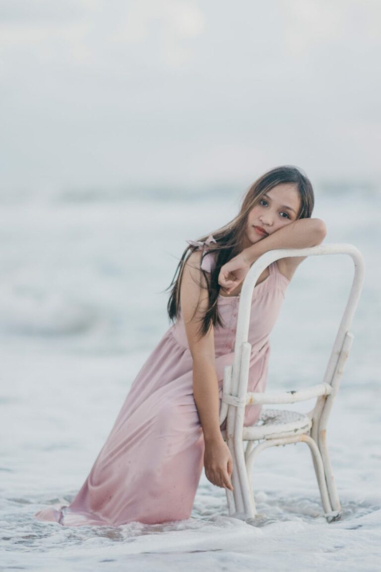 a woman in a pink dress leaning on a chair