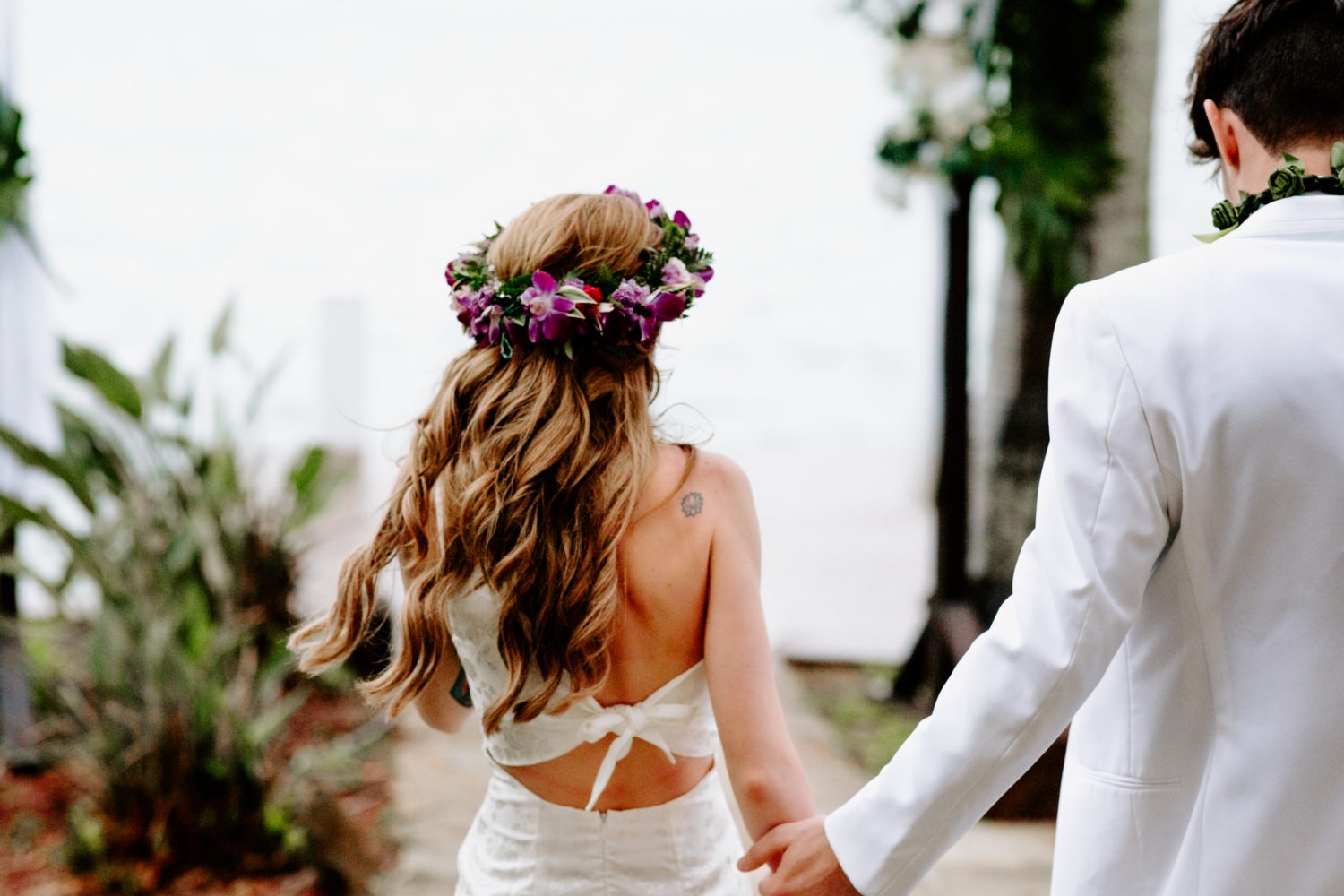 a bride and groom walking down a path holding hands